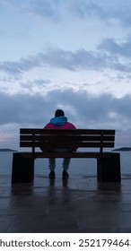 Sitting on bench by ocean at sunset, watching liquid horizon blend with dusk sky