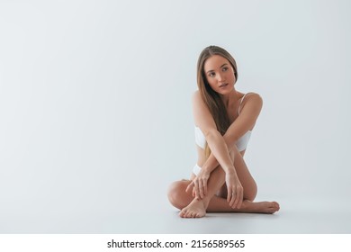 Sitting on the floor. Woman in underwear with slim body type is posing in the studio.