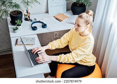 Sitting On Gym Ball At Work. Use Exercise Ball Like Chair At Workplace. Freelancer Woman Sitting On Orange Fitness Ball Using Laptop In Home Office