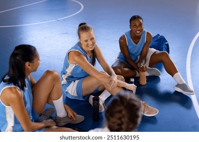 Sitting on gym floor, female basketball team members laughing and relaxing together. Teamwork, sports, camaraderie, relaxation, athletes, bonding - Powered by Shutterstock