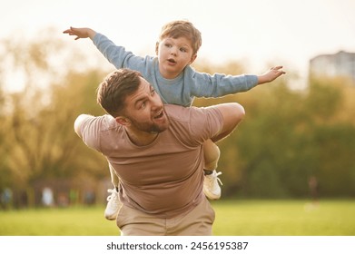 Sitting on man's shoulders. Happy father with son are having fun on the field at summertime. - Powered by Shutterstock