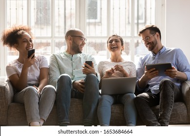 Sitting On Sofa Four Multiracial Friends Using Diverse Devices Hold Phones Laptop And Tablet Have Fun Together Chatting Enjoy Live Communication, Generation And Modern Gadgets, Social Networks Concept