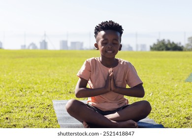 Sitting on yoga mat, african american boy meditating outdoors with hands in prayer position. Meditation, mindfulness, relaxation, serenity, tranquility, wellness - Powered by Shutterstock