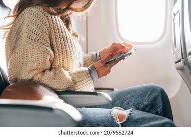 Sitting With Phone In Hands. Young Female Passanger In Casual Clothes Is In The Plane.