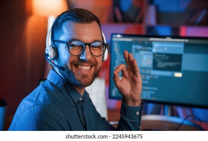 Sitting and smiling. Professional programmer is working indoors. Neon lighting.