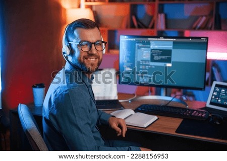 Sitting and smiling. Professional programmer is working indoors. Neon lighting.