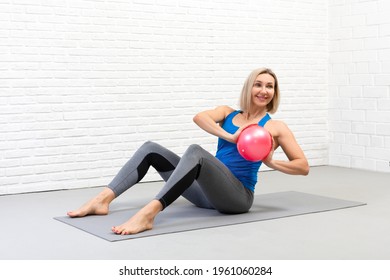 Sitting spine twisting with small fit ball. Attractive adult caucasian woman in sportswear practice pilates indoor.