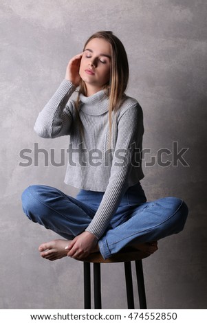 Sitting teen in pullover touching her face. Gray background