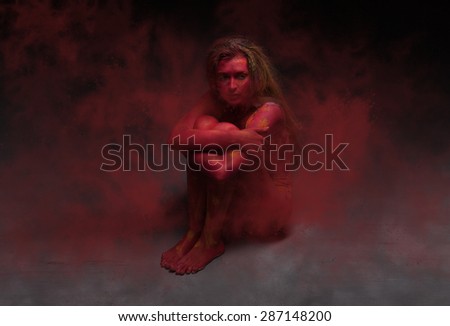 Sitting woman with body art and long hair on dark background with red  smoke