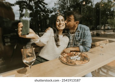 Sitting at a wooden table, a couple shares a moment of laughter as they sip colorful drinks, surrounded by a warm atmosphere and delicious pizza. - Powered by Shutterstock