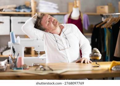 Sitting at workplace, man tailor does limbering