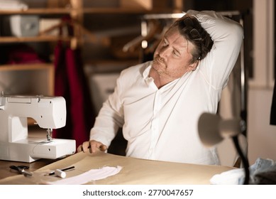 Sitting at workplace, man tailor does limbering