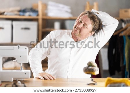 Sitting at workplace, man tailor does limbering