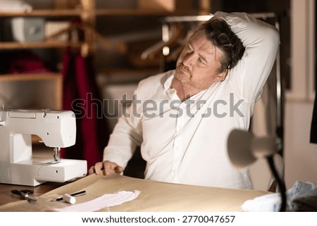 Sitting at workplace, man tailor does limbering