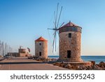 Situated on the long wave breaker at Mandraki harbour, Rhodes, Greece, stand these  medieval windmills. The fortress and the lighthouse of Agios Nikolaos (Saint Nicholas) are in the background.