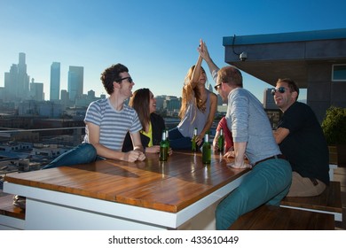 Six Adult Friends Drinking Beer At Table Of Rooftop Bar With Los Angeles Skyline, USA