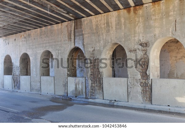 Six arches on railroad viaduct that\'s falling\
apart. Walls with spalling cement show exposed rusty reinforcement\
bar. Striped ceiling leaks rusted water clear through concrete on\
this dangerous bridge