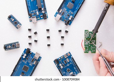 Six Arduino  boards for robotics, 3D printing or developments and inventions. A man's hand with a soldering iron. You can see smoke from rosin. Learning boards in Fablab - Arduino Nano, Uno and Mega