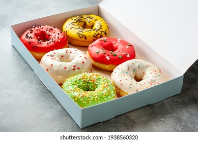 Six assorted glazed sweet donuts in a paper box on a table