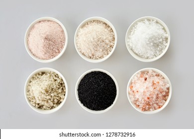 Six assorted gourmet salts in bowls with black Hawaiian lava salt, Indus salt, Fleur de sel, rock salt and sea salt viewed from above