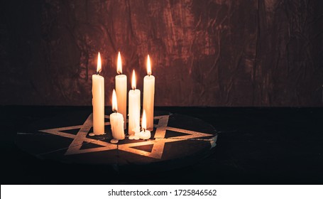 Six burning candles and the Star of David against on a red background wall.