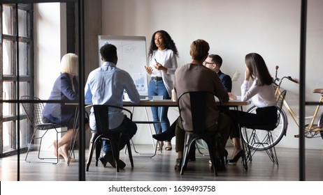 Six diverse businesspeople gathered in modern board room, different age ethnicity workers listen african woman coach tell about strategy, reporting using flip chart. Training and negotiations concept - Shutterstock ID 1639493758