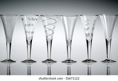 Six empty etched crystal liqueur glasses in a row, with a gray background.