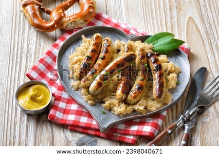 Six fried Nuremberg sausages with sauerkraut on a heart-shaped pewter plate, served with mustard and a Bavarian pretzel