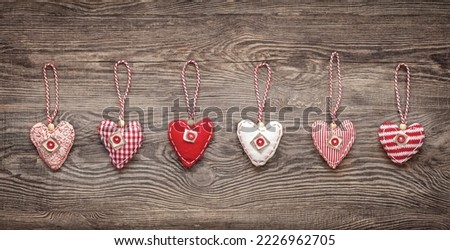 six hand-sewn fabric hearts hang on a string in front of a wooden board. rustic decoration concept.