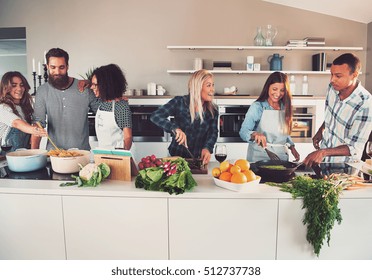 Six mixed Black and white friends preparing vegetables and pasta at long table in kitchen - Powered by Shutterstock