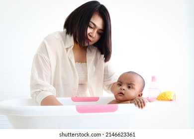 A Six Month African American Infant Baby Taking Bubble Bath In Bathroom, Mother Bathing Kid In Tub, Mom Washing And Cleaning Her Child In Bath.