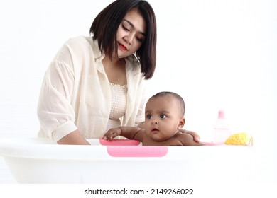 A Six Month African American Infant Baby Taking Bubble Bath In Bathroom, Mother Bathing Kid In Tub, Mom Washing And Cleaning Her Child In Bath.