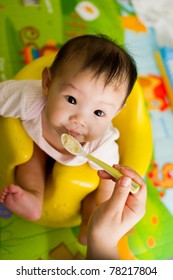 Six Month Old South East Asian Chinese Baby Girl Sitting In A Yellow Seat, Being Spoon Fed