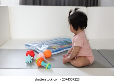 Six Months Old Asian Baby Girl Sitting On Futon Surrounding With Colorful Baby Toys.