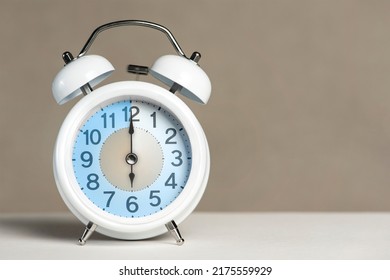 Six o'clock on the alarm. A white alarm clock is on a white table. The clock hand points to 6 o'clock. Time to change to summer or winter time. Set an alarm for 6:00 or 18:00. copy space