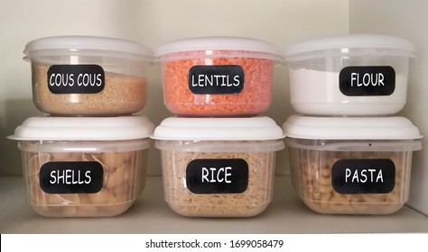 Six Plastic Containers With Dry Food (couscous, Red Lentils, White Flour, Pasta Shells, Rice, Elbow Pasta) In The Kitchen Cupboard.