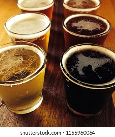 Six Small Full Glasses Of Craft Beer Arranged On A Wooden Tasting Paddle