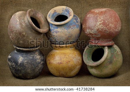 six small plant clay pots (mass produced planters) with rough color finish on dark burlap texture background, still life