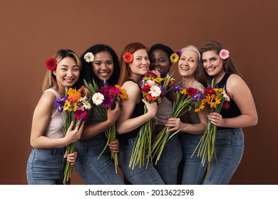 Six Smiling Women Of Different Ages Looking At Camera In A Studio. Happy Diverse Females With Bouquets And Flowers In Their Hairs Standing Together.