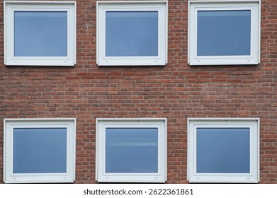 Six square windows with white frames are set in a red brick wall, reflecting the blue sky