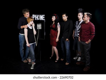 Six Teenagers In A High School Play.  A Group Of Teenagers Wait For Their Turn To Use A Public Phone, While Another Girl Hogs It.