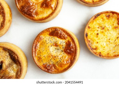 Six Traditional Hot Baked Meat Pies With Golden Pastry Crusts On White Marble Texture Kitchen Counter From Overhead Flat Lay 
