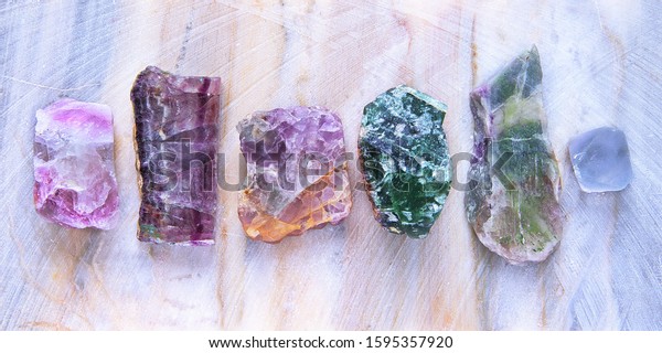 Six\
translucent samples of fluorite mineral stones on marble plate\
close-up. Macro shooting of specimens of natural mineral fluorite\
crystal of various colors as a\
background.