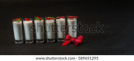 six white coconut drinks decorated with red and green peppers lined up, decorated with a bow on the right, all on a black background, drink set