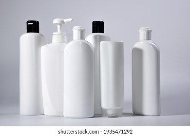 Six white plastic bottles with shampoo and conditioner and shower gel on a white background.