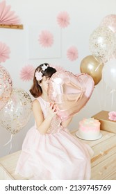 Six Year Girl Wearing Dress Holding Light Pink Heart Shaped Balloon. Home Birthday Party