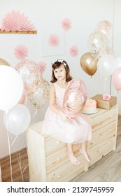 Six Year Girl Wearing Dress Holding Light Pink Heart Shaped Balloon. Home Birthday Party