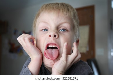 A six year old boy child is being funny and making a bratty face while sticking out his tongue.