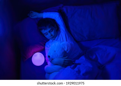 Six Years Old Bouy Sleep With LED Night Lamp, School Child Dreaming And Holding Plush Toy. Kid Angry Of Darkness.