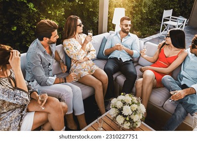 Six young Caucasians, three men and three women, sitting in an elegant outdoor setting, casually chatting and enjoying champagne. The shot is taken from above. - Powered by Shutterstock